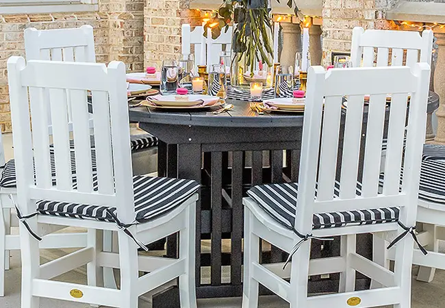 White poly chairs sitting at a black poly table. The table is set for a meal and it is a cozy atmosphere with hanging accent lights.